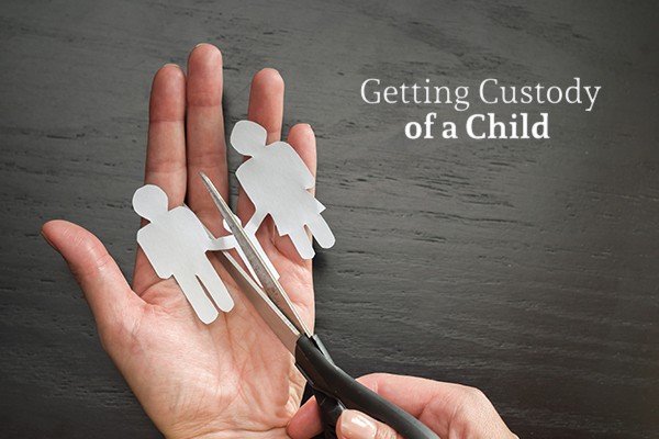 A person holds a paper cutout of three people with a pair of scissors about to cut one of the "parent" people cutouts from the other two beside the words "Getting Custody of a Child"